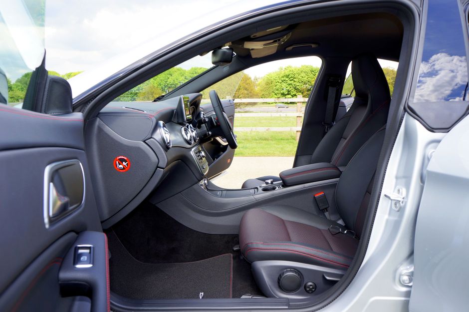 Interior of a vehicle showing white leather rear seats with three headrests, seat belts, and black seat belt buckles. The black door panel with a silver handle is visible on the left, and the back of
